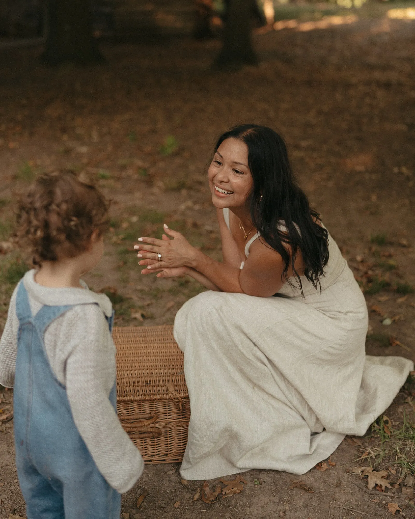 Angela crouched beside a picnic basket, laughing with a toddler in overalls