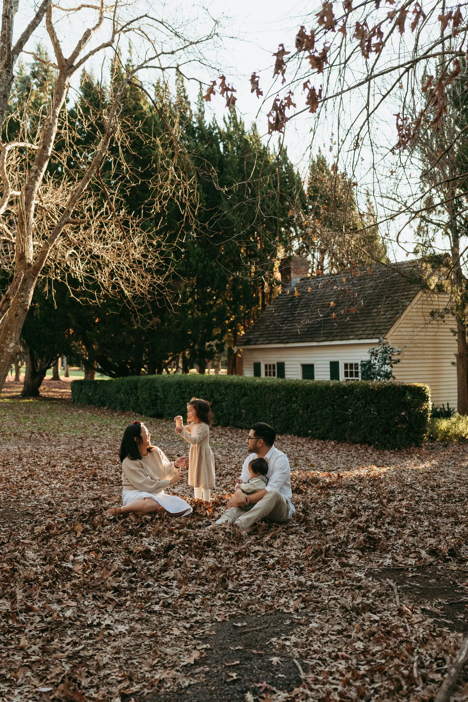 A family sitting in autumn leaves in front of a white cottage