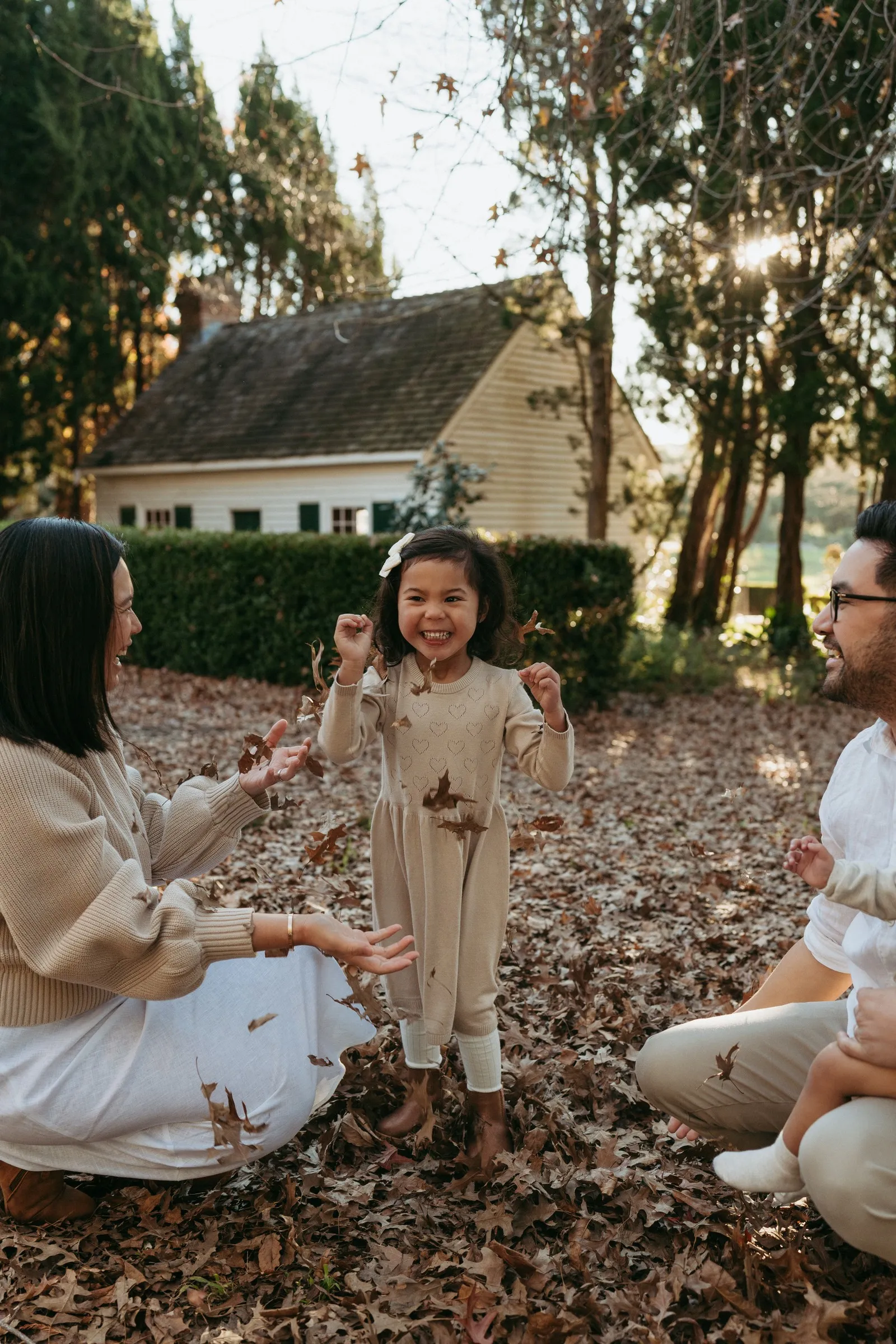 A smiling little girl playing in autumn leaves with her family