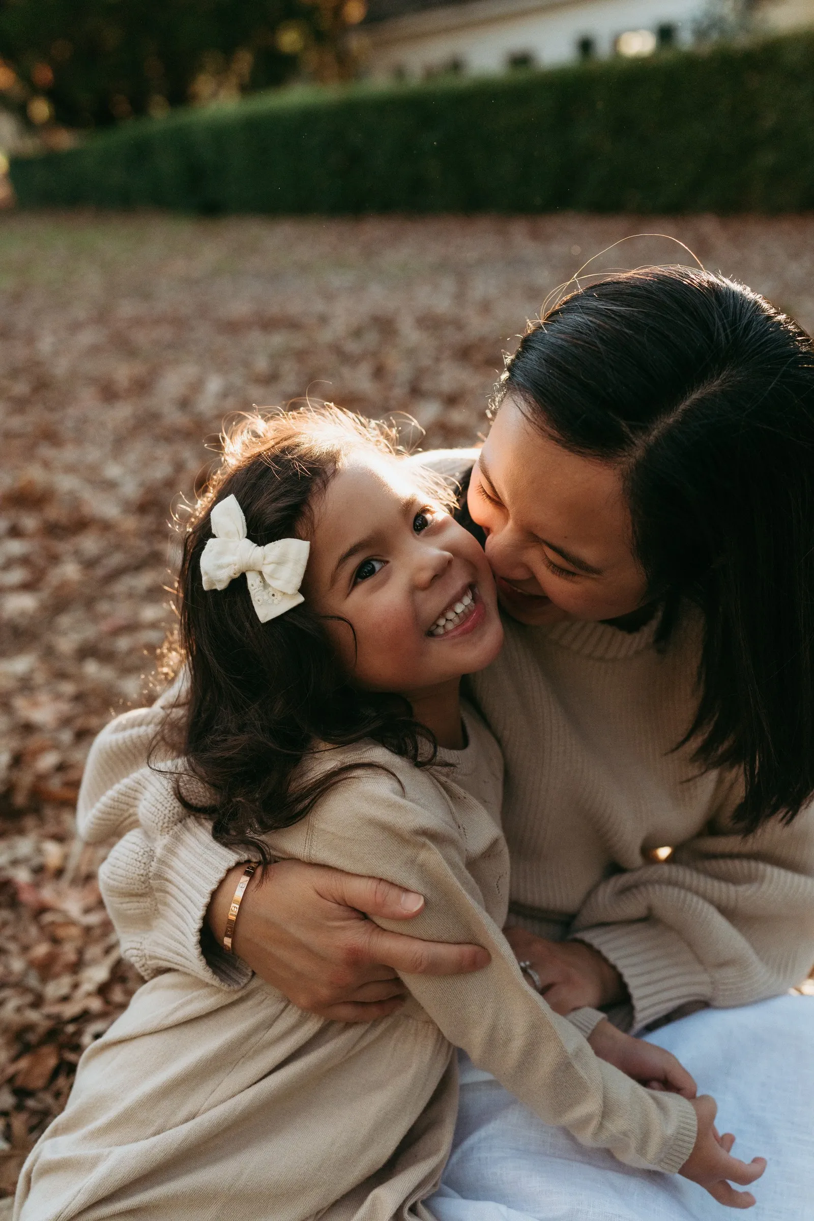 A mum kissing her smiling daughter’s cheek in the autumn leaves