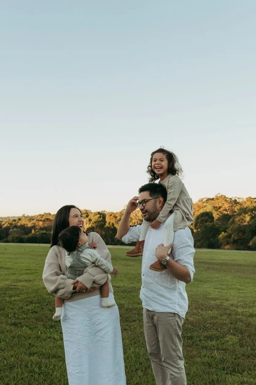 A dad carrying his daughter on his shoulders beside mum and baby