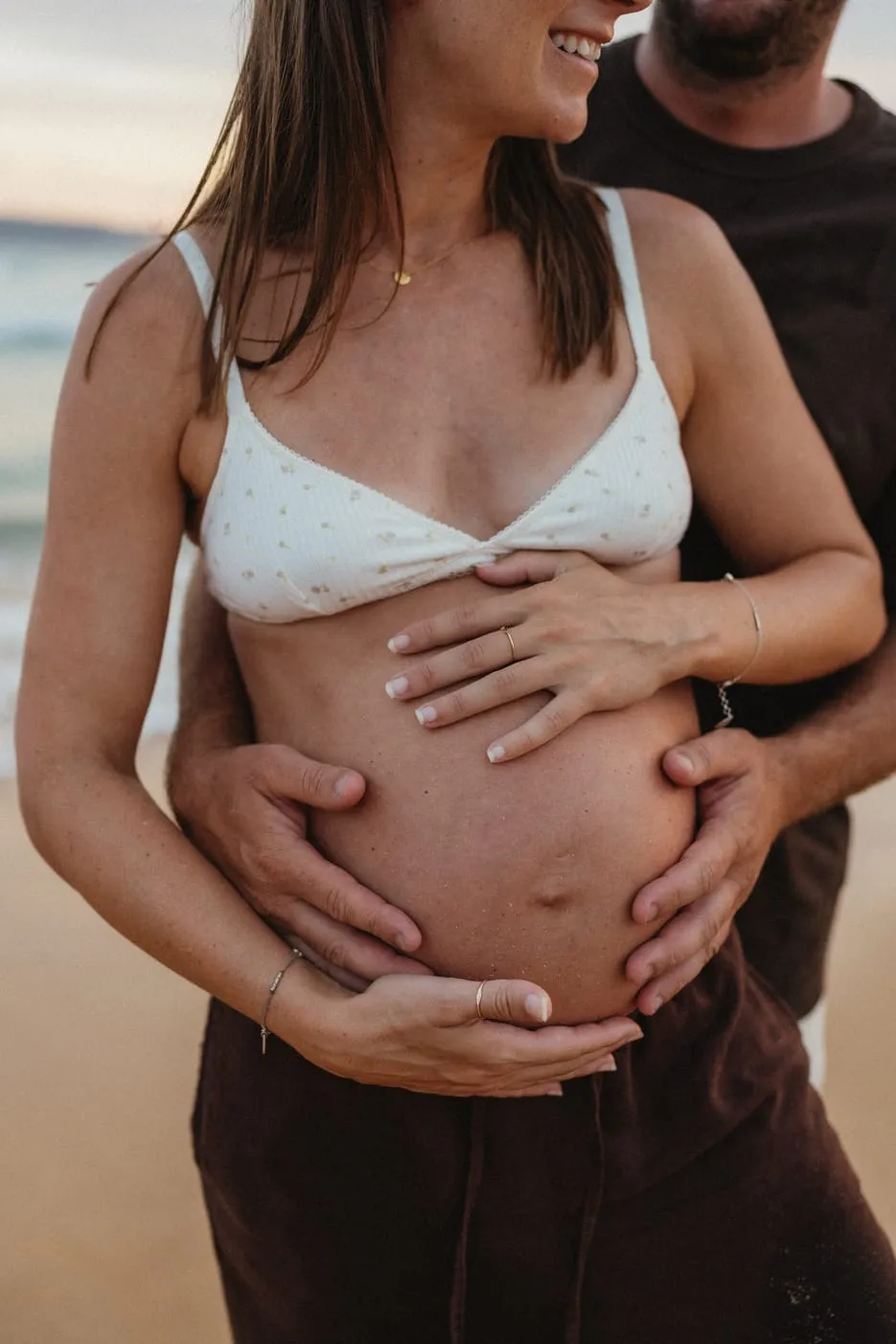 Hands resting on a pregnant belly at the beach