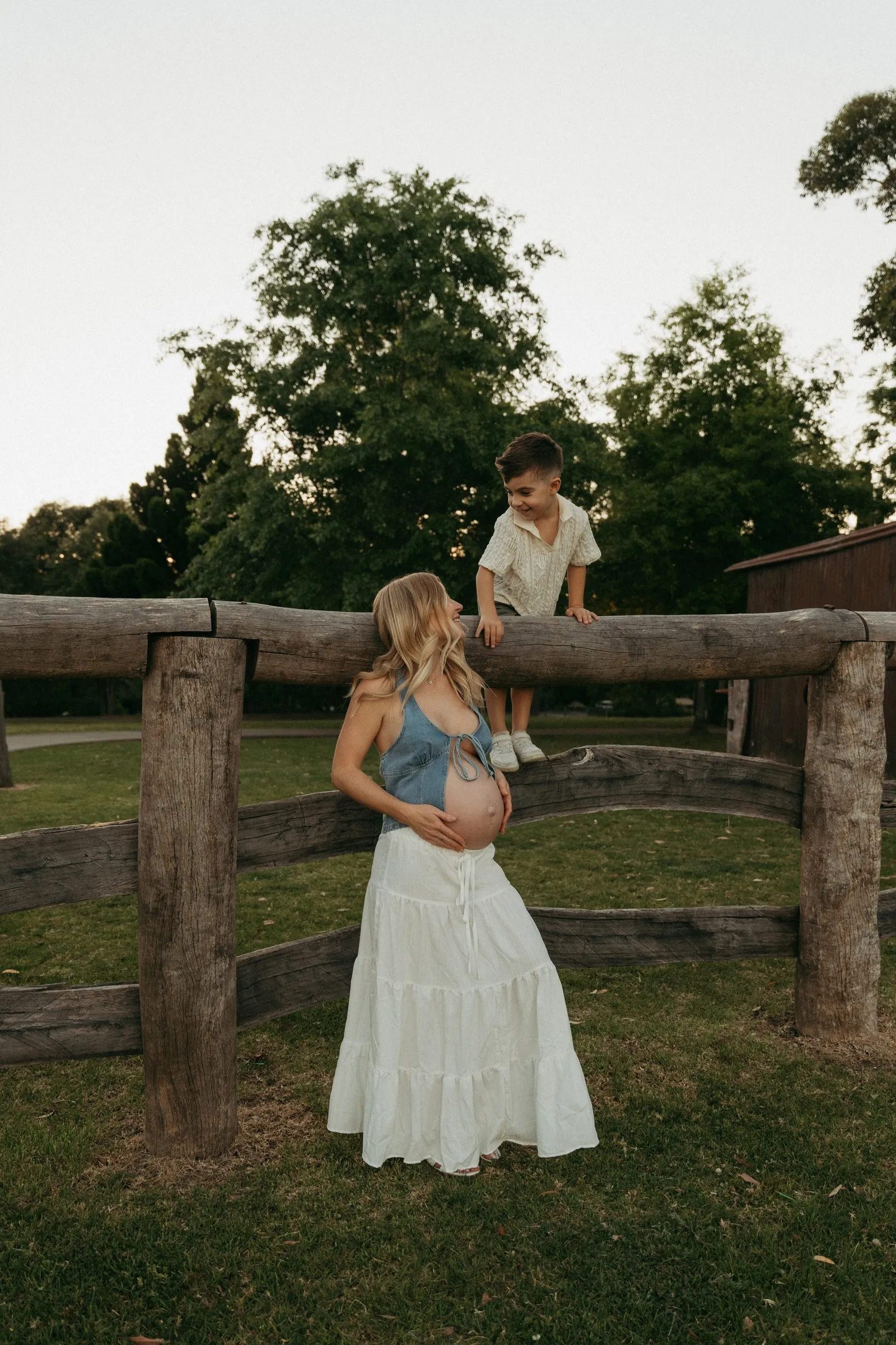 An expecting mum holding her little boy beside a wooden fence