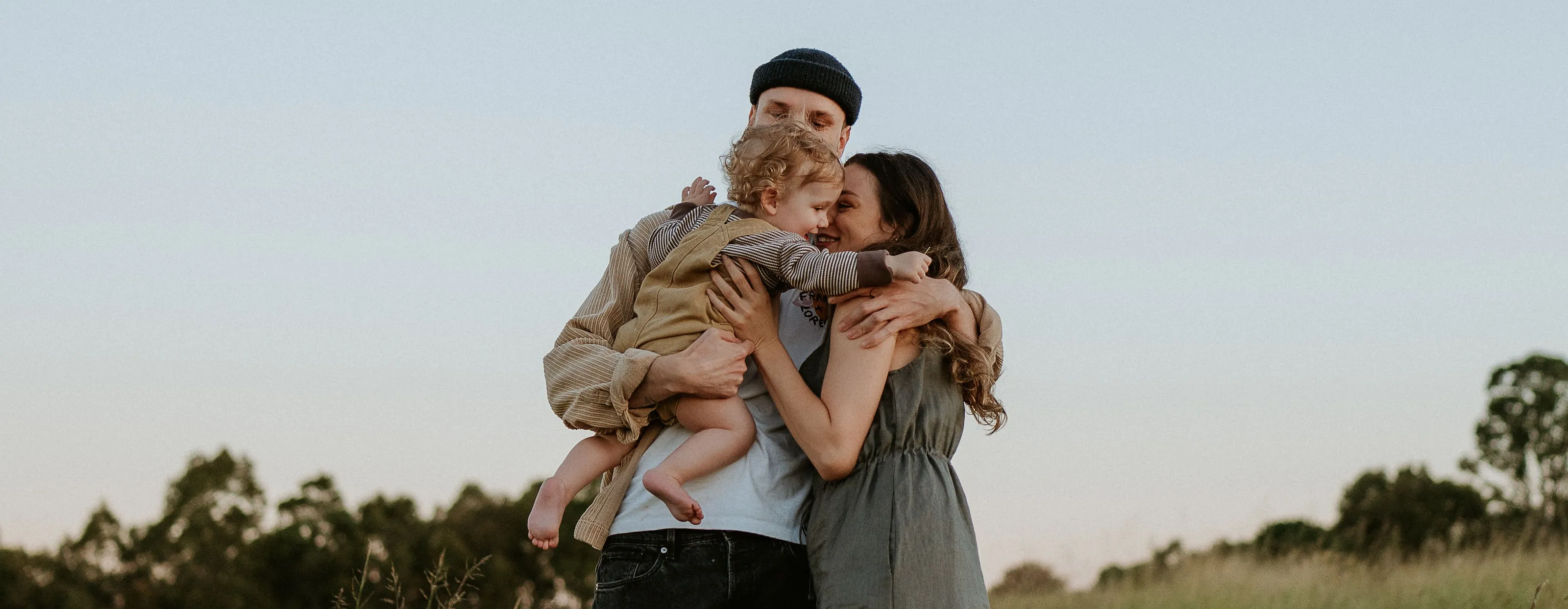 Parents hugging their little one in a green meadow