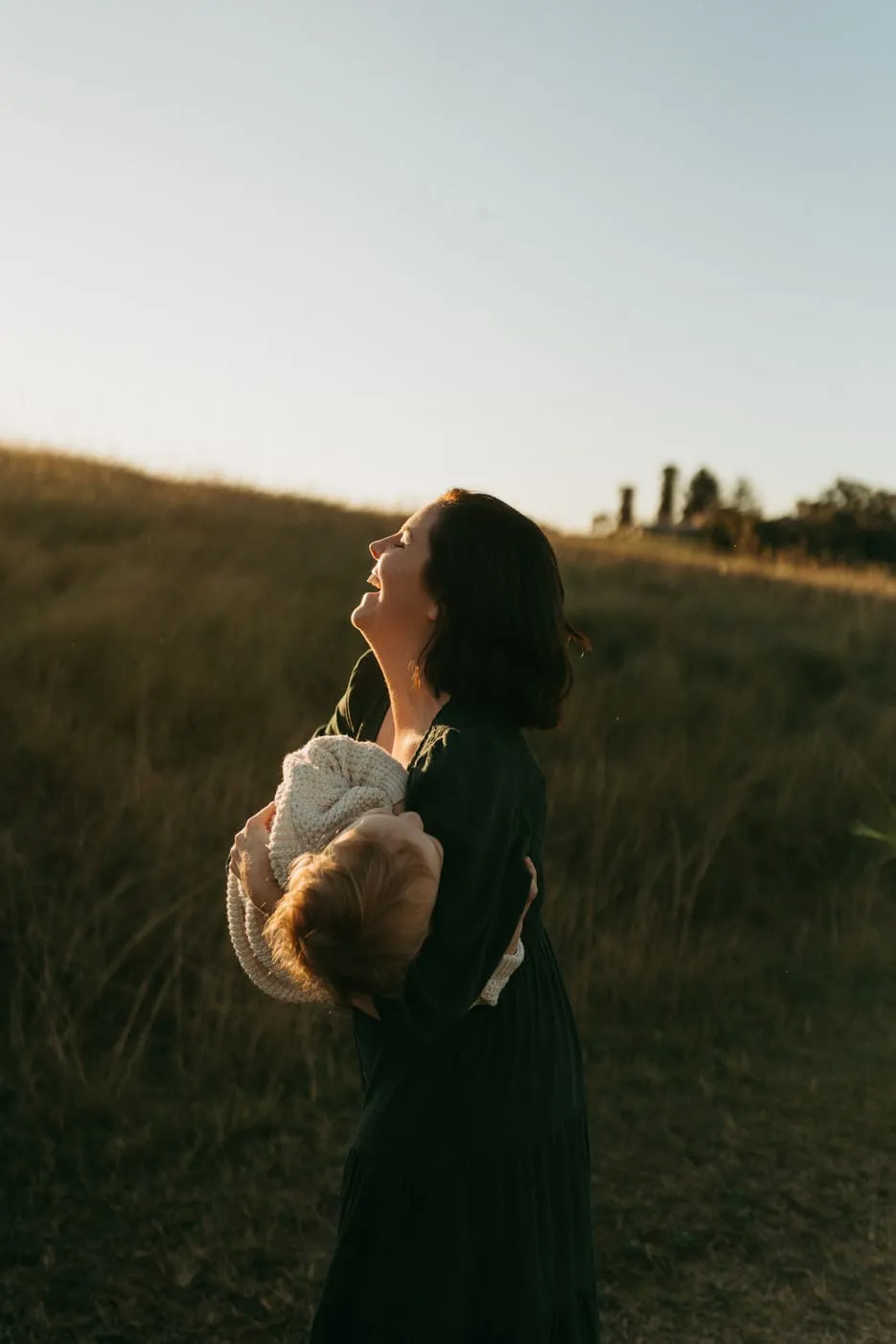 A mum lifting her little one high in a golden field