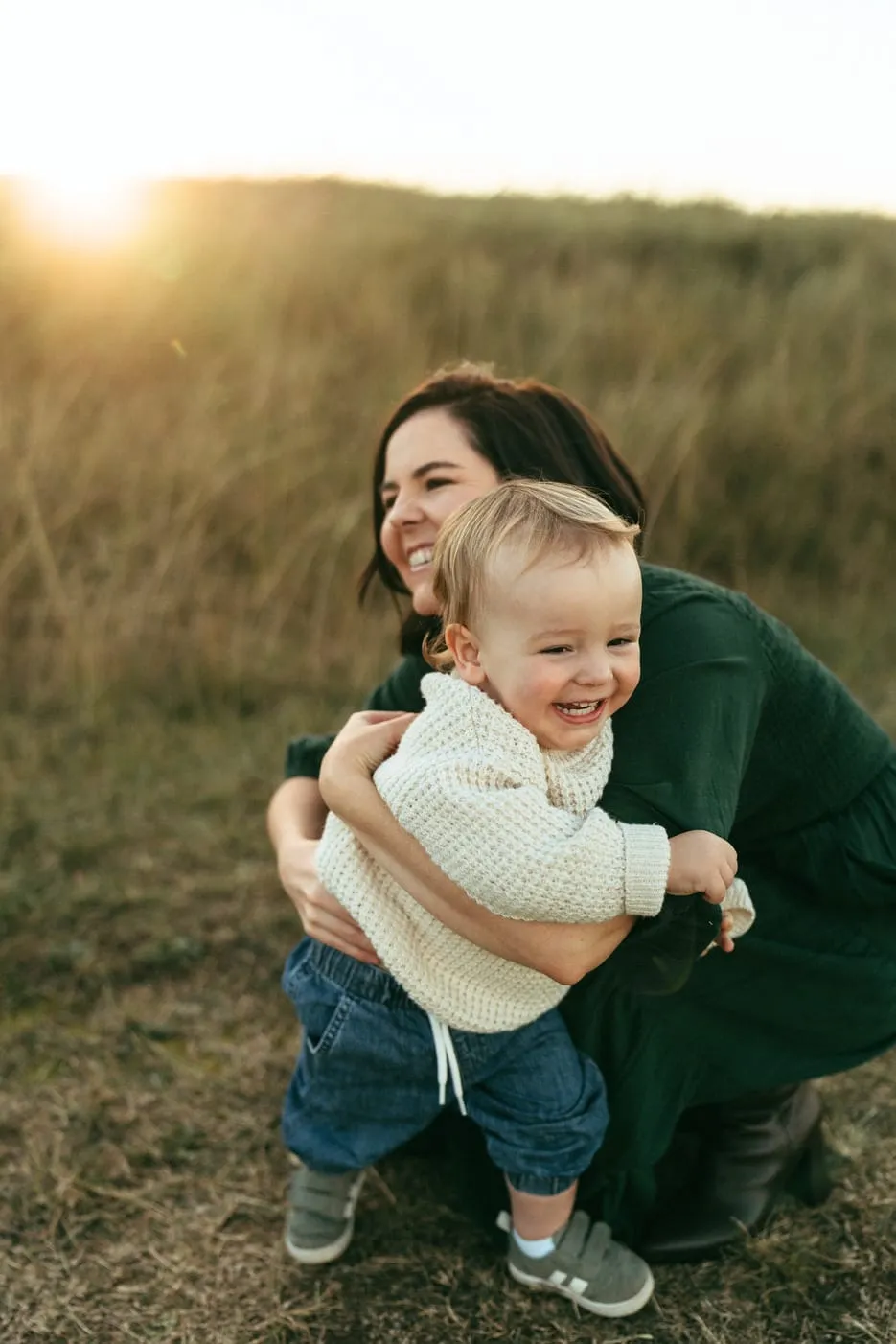 A mum and her toddler hugging and laughing in the grass