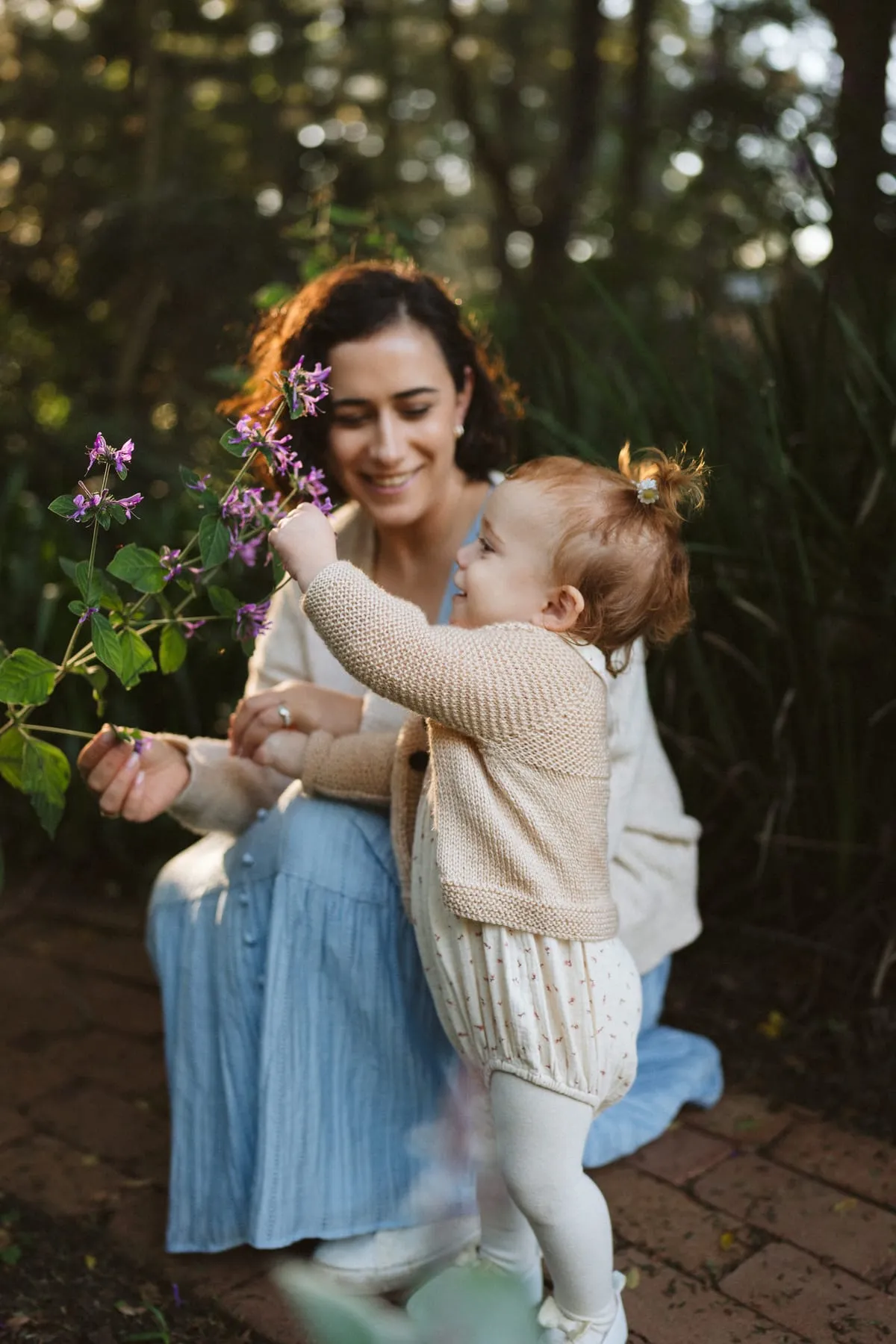 A mum holding her toddler beside a flowering garden